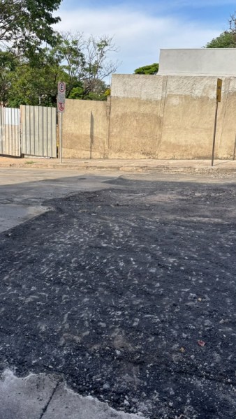 Vista de uma esquina com asfalto danificado e cercas ao fundo, incluindo um sinal de trânsito.