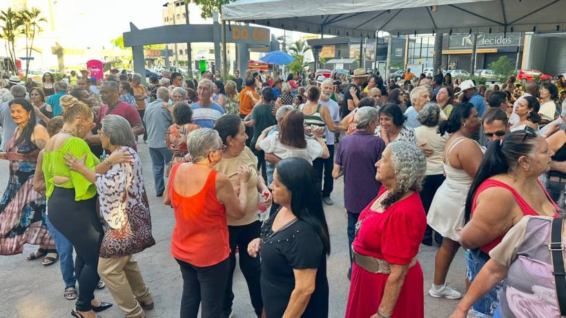 Grupo de pessoas dançando e se divertindo em um evento ao ar livre, com muitas mulheres e homens de várias idades, em um ambiente urbano.