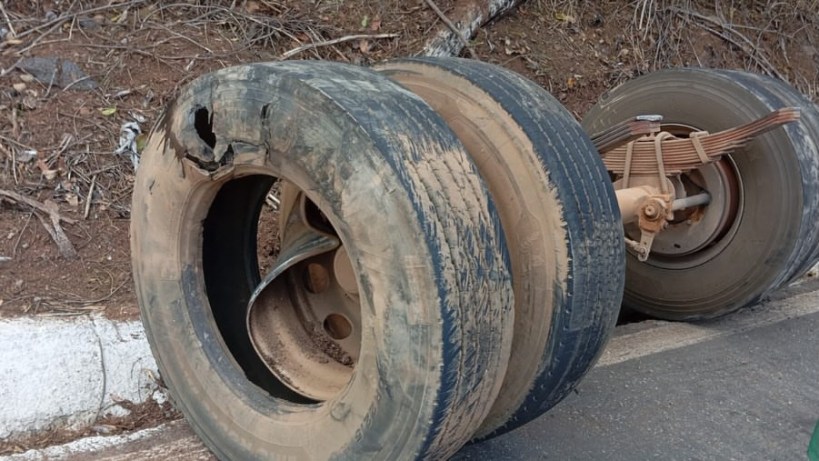 Pneu danificado de um caminhão em uma estrada, com desgaste visível e buraco na lateral.