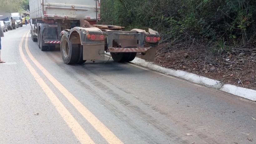 Caminhão parado em uma estrada com marcas de pneus visíveis e vegetação ao lado.