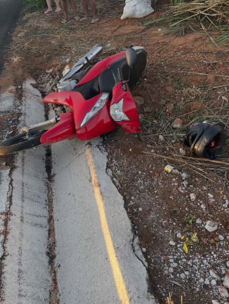 Uma moto vermelha caída ao lado da estrada, com um capacete preto próximo a ela.