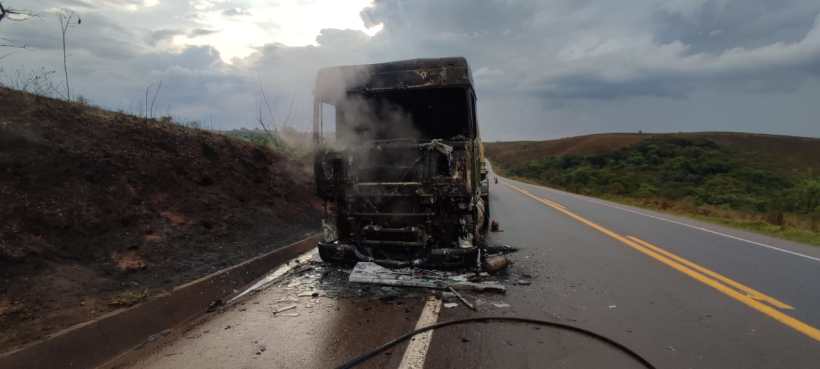 Caminhão queimado parado na estrada, com fumaça saindo do motor e área ao redor desolada.
