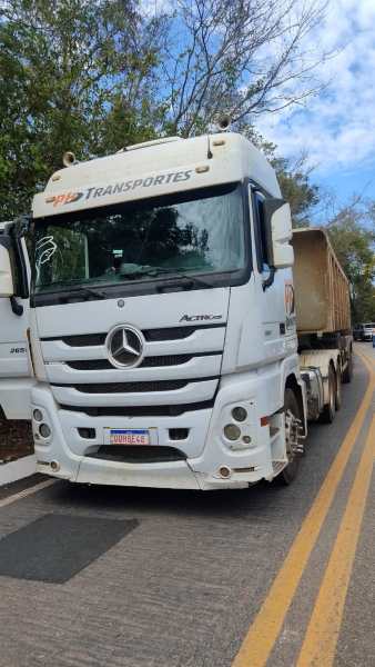 Caminhão Mercedes-Benz Actros na estrada, com a cabine branca e a carga visível atrás.