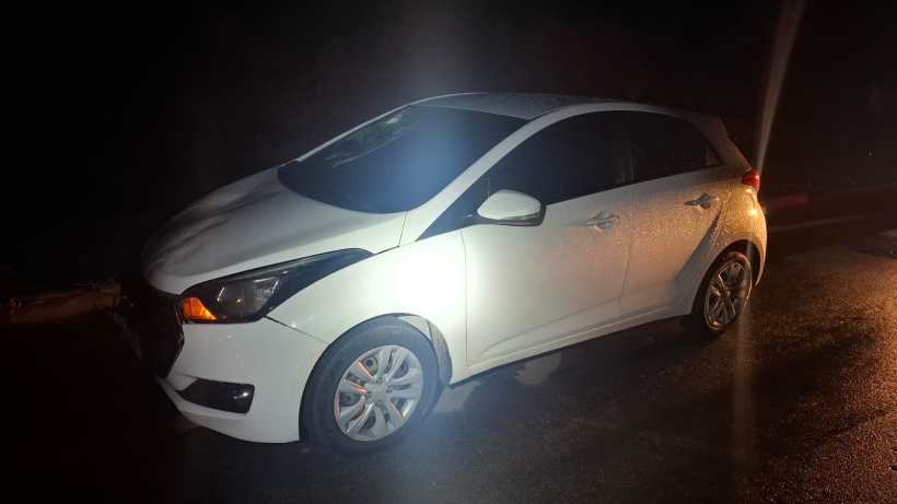 Carro branco estacionado à noite, iluminado por faróis.