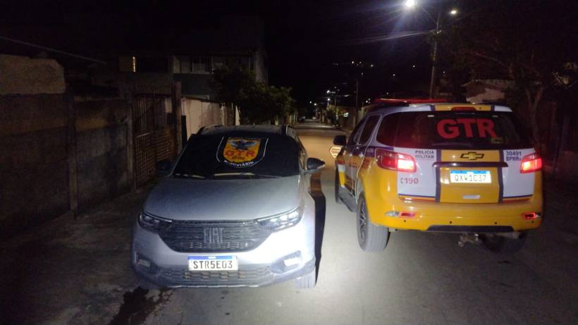 Veículos de polícia estacionados em uma rua à noite, um carro cinza à frente com um emblema da GTR.
