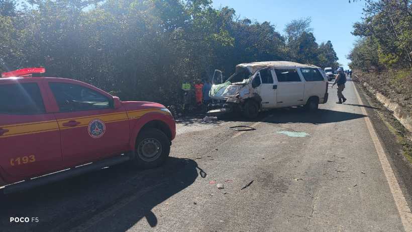Veículo utilitário destruído em acidente na estrada com bombeiros e emergência ao fundo.