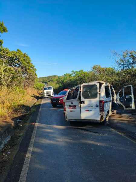 Acidente de trânsito com uma van branca e um carro vermelho parados em uma estrada rural, cercados por vegetação.
