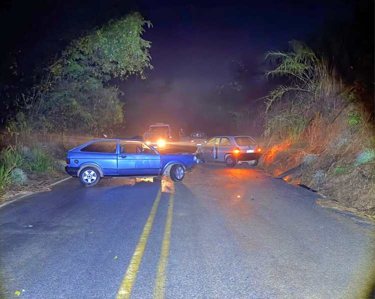 Caminho obstruído por veículos em uma estrada à noite, com um carro azul e outros veículos parados.