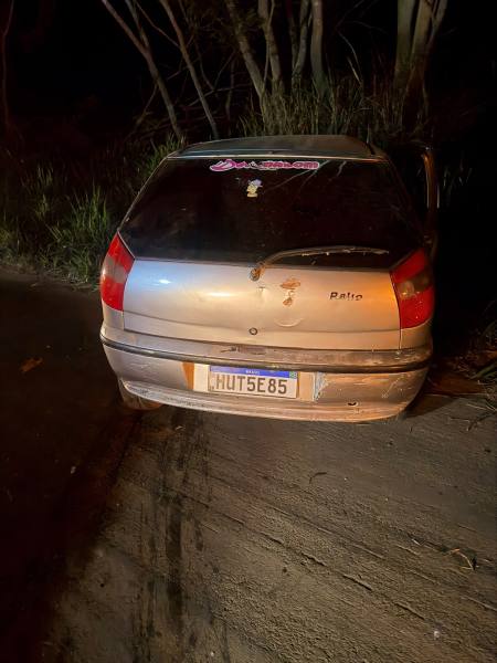 Um carro prateado estacionado à noite, com um adesivo rosa na janela traseira e visíveis sinais de desgaste.