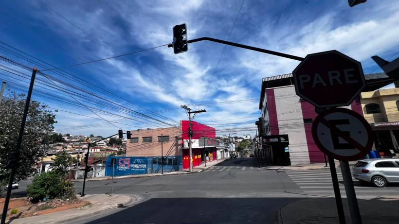 Imagem de uma interseção urbana com semáforo e placas de trânsito, incluindo uma placa de pare, sob um céu azul com nuvens.