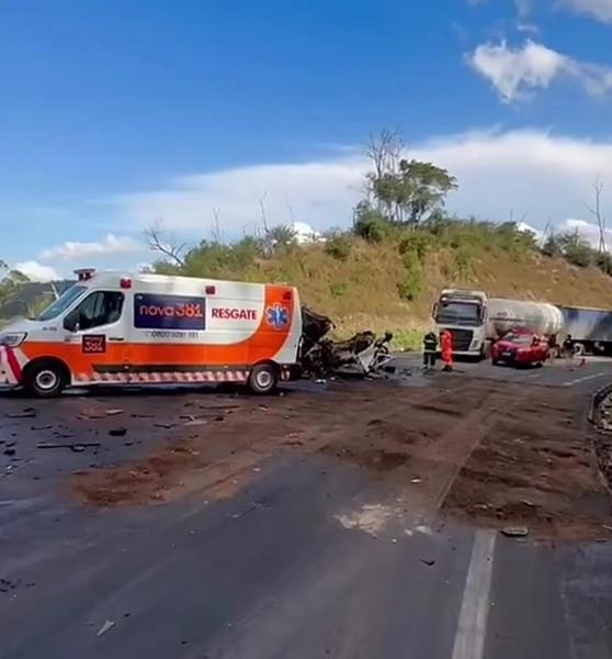 Acidente de trânsito com veículos danificados, incluindo uma ambulância e um caminhão, em uma estrada com céu azul ao fundo.