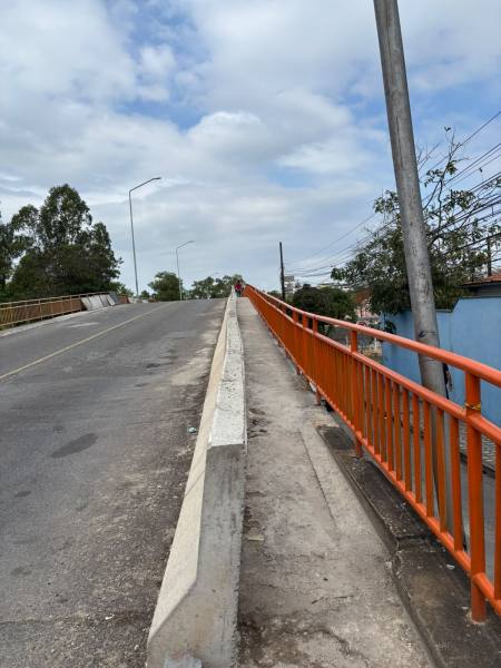 Vista de uma ponte elevada com guardrails laranja, mostrando uma estrada em subida sob um céu nublado.