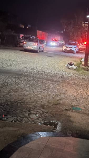 Rua à noite com carros de polícia e iluminação vermelha, mostrando uma cena de atividade policial.