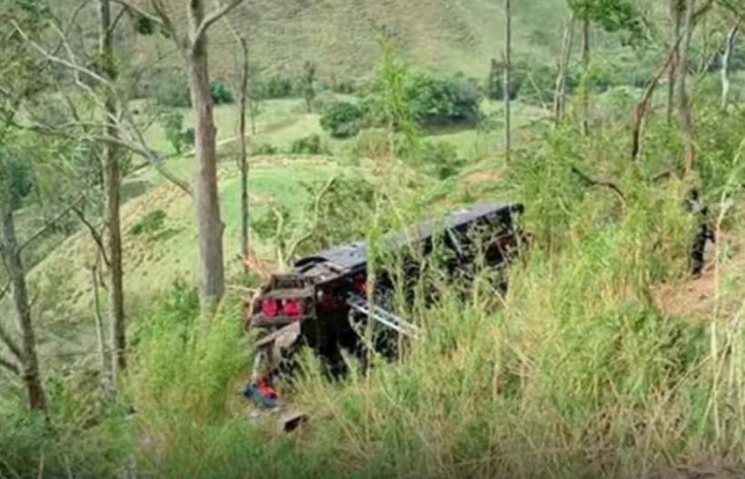 Caminhão tombado em uma encosta, cercado por vegetação densa e árvores.