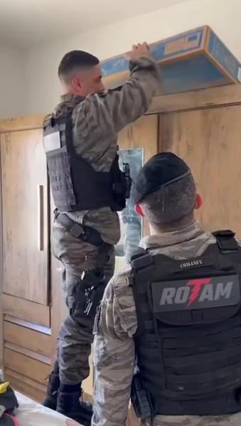 Policiais militares buscando algo em um armário em um ambiente residencial.