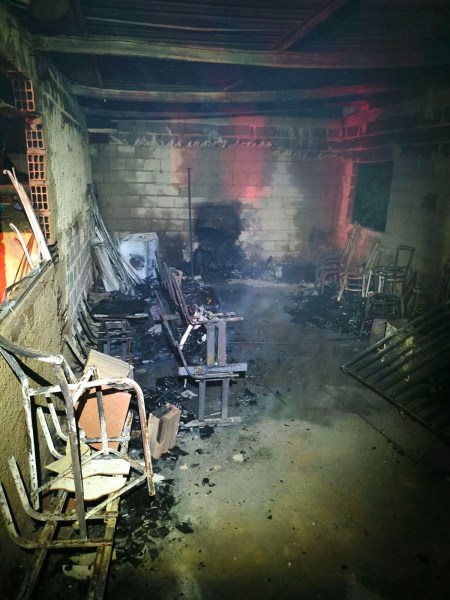 Interior de um espaço com marcas de incêndio, apresentando móveis danificados, incluindo cadeiras e resíduos de material queimado.