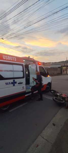 Uma ambulância do SUS parada na rua, com um profissional de saúde saindo do veículo enquanto uma motocicleta caída está ao lado.