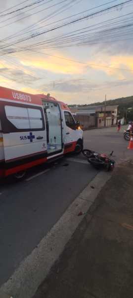 Uma ambulância parada ao lado de uma motocicleta caída em uma rua urbana, ao entardecer.