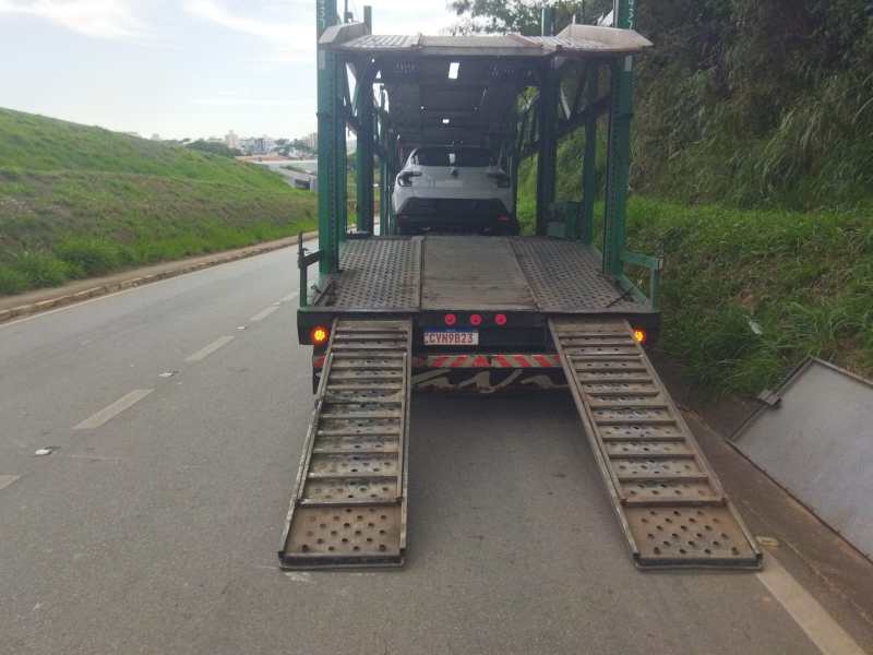 Caminhão transportando carros com rampas de acesso, estacionado em uma estrada.
