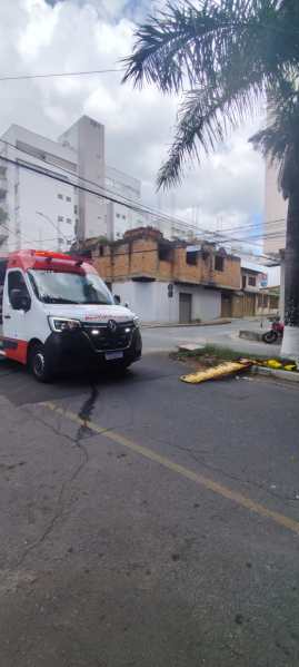 Uma ambulância parada em uma rua, com prédios ao fundo, e uma palmeira à direita.