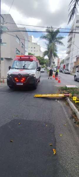 Ambulância parada em uma rua, com cones de sinalização e uma placa no chão.