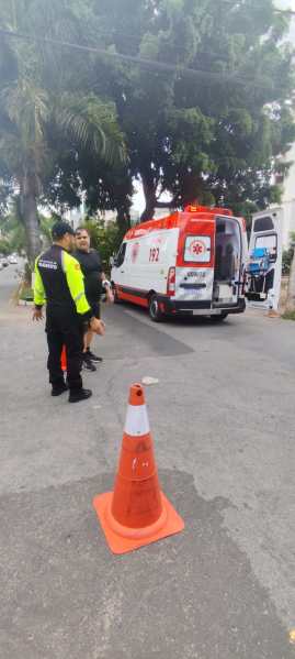 Uma ambulância de emergência com a matrícula 192 estacionada na rua, com dois homens, um vestido de uniforme de polícia e outro em roupas civis, conversando próximo a um cone de sinalização.
