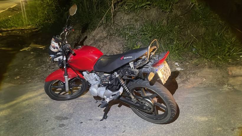 Motocicleta vermelha da marca Honda estacionada à beira da estrada à noite.
