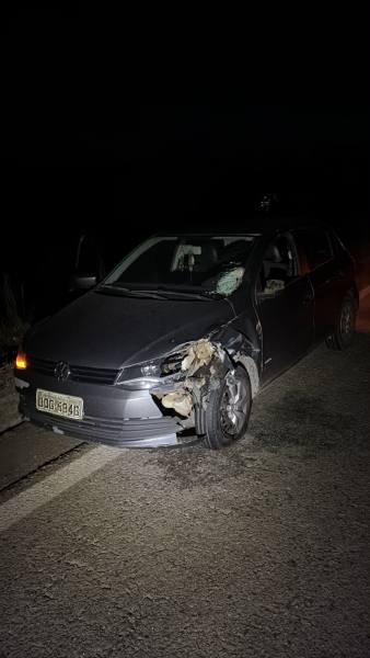 Carro acidentado à noite, com danos visíveis na lateral e no para-brisa.