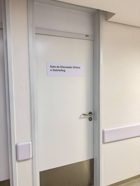 Porta da sala de discussão clínica e debriefing com sinalização visível.