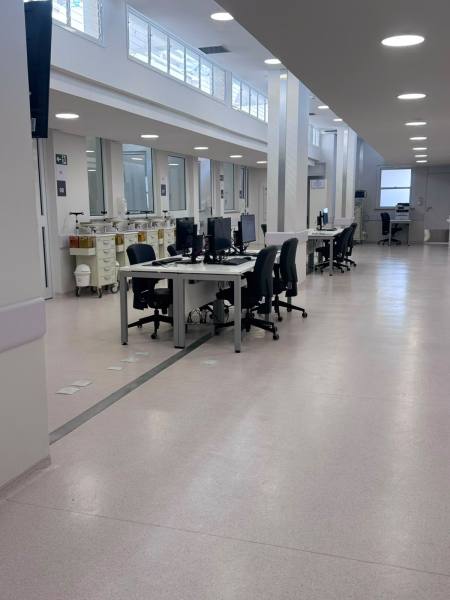 Visão interna de um escritório moderno com mesas de trabalho, computadores e cadeiras, em um ambiente bem iluminado.