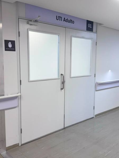 Portas brancas de entrada para a UTI Adulto, com janelas de vidro e sinalização acima.
