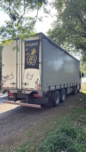 Caminhão baú parado à beira da estrada, visto de costas, com uma logo na parte traseira.
