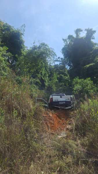 Carro abandonado em uma trilha de terra cercada por vegetação densa
