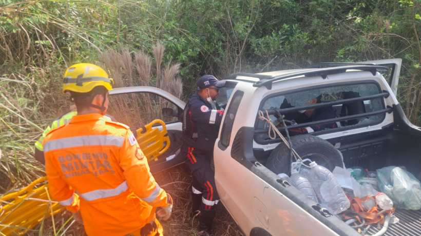 Equipes de resgate trabalham para ajudar pessoas em um veículo acidentado na vegetação.