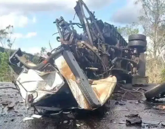 Caminhão capotado na estrada, com danos visíveis e entulho ao redor.