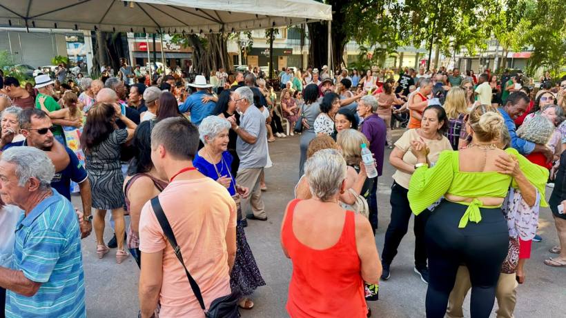 Uma multidão de pessoas dançando em um evento ao ar livre, com diversas idades e estilos de roupas, sob uma tenda.