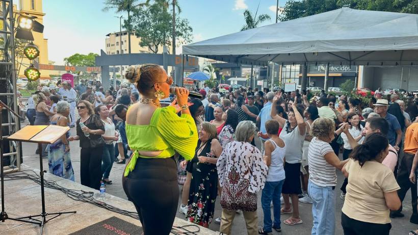 Cantora se apresenta em um palco, enquanto uma multidão de pessoas dança e se diverte ao seu redor em um evento ao ar livre.