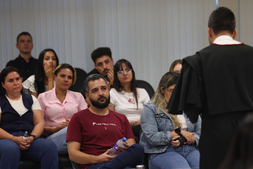 Um grupo de pessoas atentas em uma sala, com um homem vestido de toga falando para a audiência.