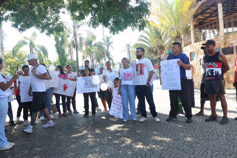 Grupo de pessoas protestando em um espaço ao ar livre, segurando cartazes e balões brancos, em apoio a uma causa social.