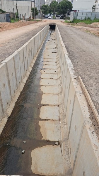 Canal de drenagem em uma rua, com pisos de concreto e água acumulada.