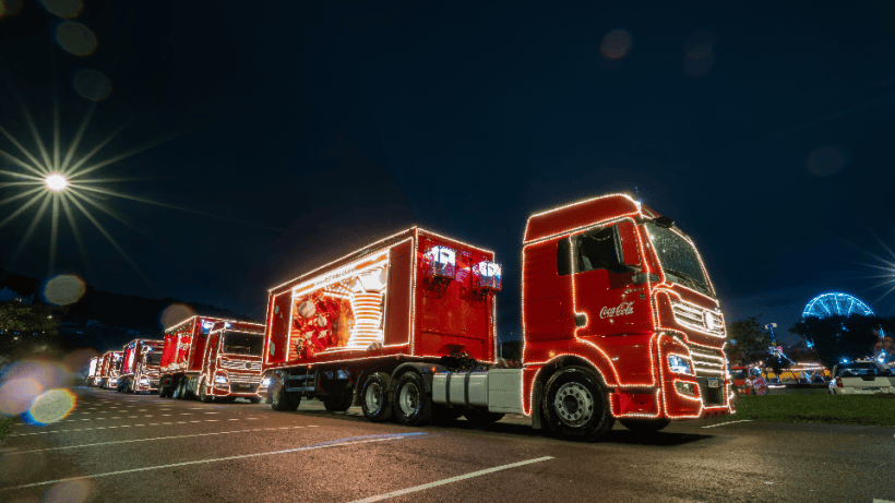 Caminhões vermelhos da Coca-Cola decorados com luzes brilhantes em um evento noturno.