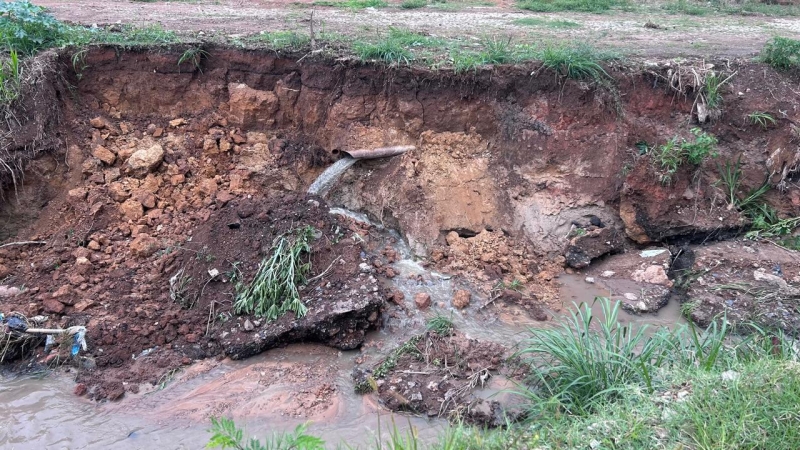 Imagem de um deslizamento de terra com um tubo de drenagem, onde a água é despejada em uma área de barro e grama ao redor.