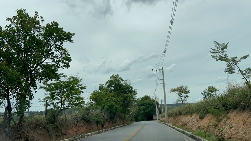 Estrada rural cercada por árvores e postes de eletricidade sob um céu nublado.