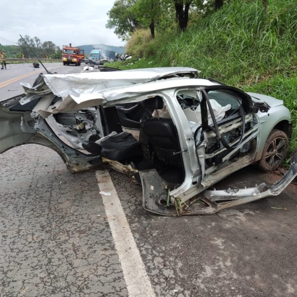 Carro destruído após acidente na estrada, com a parte lateral danificada e assentos visíveis.
