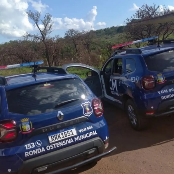 Dois carros de patrulha da Ronda Ostensiva Municipal estacionados em uma estrada de terra, com céu parcialmente nublado ao fundo.