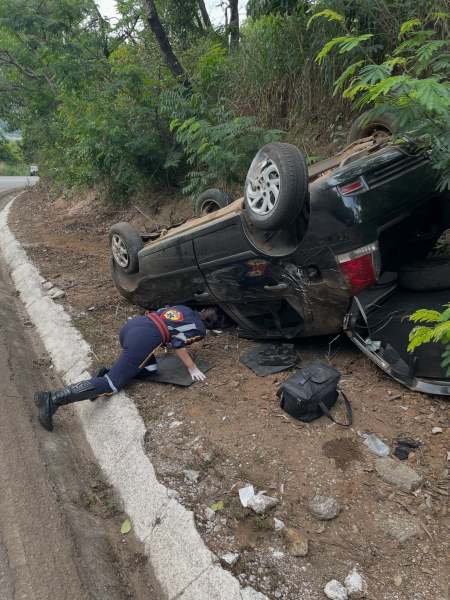 Veículo tombado na beira da estrada com socorrista prestando assistência.