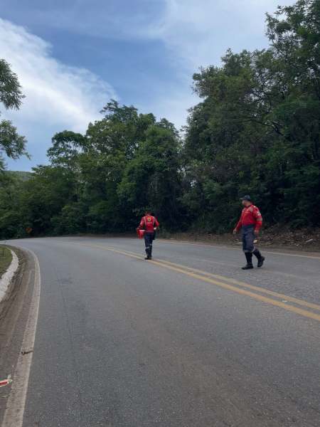 Dois homens vestidos de vermelho caminhando ao longo de uma estrada cercada por árvores.