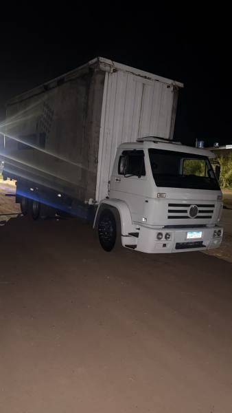 Caminhão branco estacionado à noite, com baú grande e fundo iluminado.