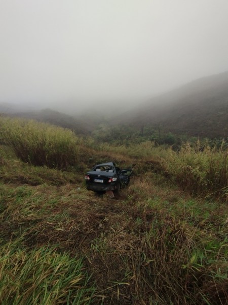 Um carro preto paralisado em uma ladeira coberta de grama alta em meio a um cenário de neblina densa.