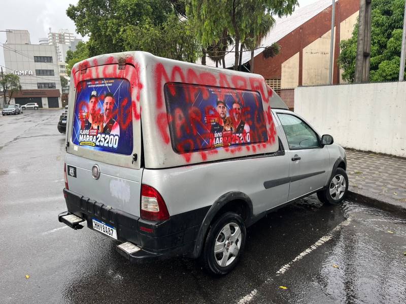 Van prata com propaganda de candidato, grafite vermelho e chuva.